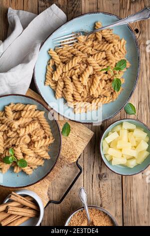 Einfache Fusilli-Pasta mit süß gebratenem Grieß und Zimt, serviert mit Ananasstücken Stockfoto