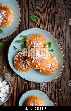 Bade Buns, klassisch englischer süßer Teig mit Sirup glasiert, gekrönt mit Kümmel Samen und zerdrückten Zuckerwürfel auf rustikalem Holzhintergrund Stockfoto