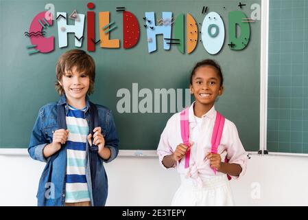 Schuljunge mit Rucksack stehen in der Nähe afroamerikanischen Freund und Kreidetafel im Klassenzimmer, Kindheit Illustration Stockfoto