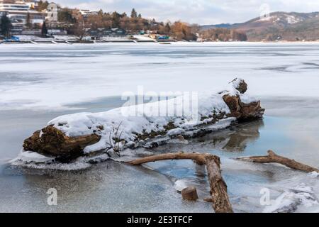 Nahaufnahme des mit Schnee bedeckten Baumstamms auf der gefrorenen Wasseroberfläche des Brünner Stausees am Fluss Svratka. Stockfoto