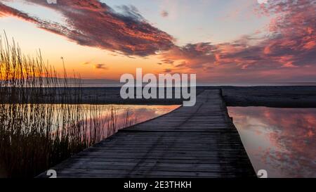 Schöner Sonnenuntergang. Rosa, goldene, orange, blaue Farben über dem Meer. Himmel voller Farben. Brücke über einen kleinen See, wo der Himmel reflektiert wird. Stockfoto