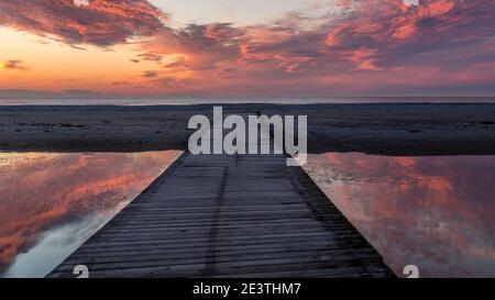 Schöner Sonnenuntergang. Rosa, goldene, orange, blaue Farben über dem Meer. Himmel voller Farben. Brücke über einen kleinen See, wo der Himmel reflektiert wird. Stockfoto