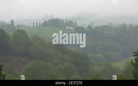 Neblige Morgenlandschaft im französischen Baskenland. Traditionelles Bauernhaus und Hügel versteckt im Nebel. Stockfoto