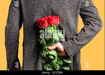 Mann mit einem Strauß roter Rosen hinter seinem Rücken. Eleganter Mann mit roten Rosenblüten in der Hand. Romantisches und Valentinstag Urlaubskonzept Stockfoto