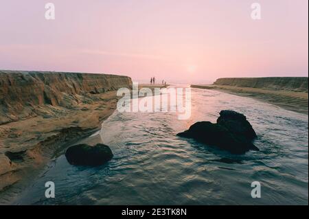 Sonnenuntergang über dem Arabischen Meer und Fluss fließt landeinwärts von Sandbänken bei Flut entlang Strand in der Nähe Kannur, Kerala, Indien flankiert. Stockfoto