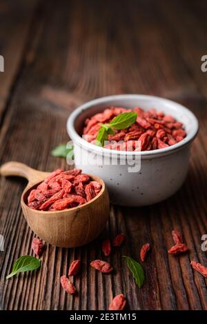 Gesunder Snack reich an Antioxidantien und Vitaminen zur Stärkung der Immunität, getrocknete Goji-Beere in einer Schüssel und Schaufel auf rustikalem Holzhintergrund Stockfoto