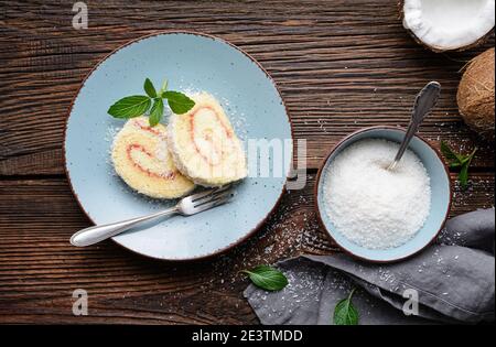 Köstliches Dessert, Kokosnussroulade Scheiben gefüllt mit Vanille und Rum Buttercreme auf rustikalem Holzhintergrund Stockfoto