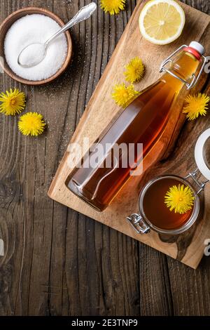 Hausgemachter gesunder Löwenzahn-Sirup in einer Glasflasche, dekoriert mit frischen Blumen auf rustikalem Holzhintergrund Stockfoto