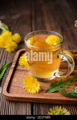 Kräutergetränk zur Leberentgiftung, Löwenzahn-Wurzeltee in einer Glasschale mit frischen Blumen auf einem rustikalen Holzhintergrund dekoriert Stockfoto