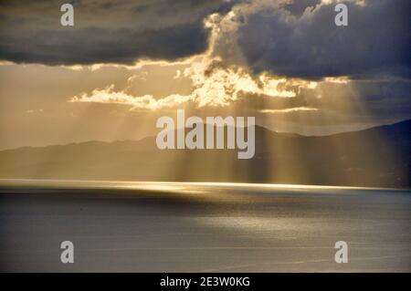 Die Sonne hinter den Wolken mit Lichtstrahlen, die auf das Meer herabscheinen. Sonnenstrahlen blicken durch Wolken auf die Adria vor Rijeka, Kroatien Stockfoto