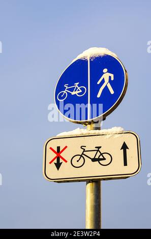 Schneebedecktes Fahrrad und Fußgängerweg rund Straßenschild auf Stange, blauer Himmel Hintergrund Stockfoto