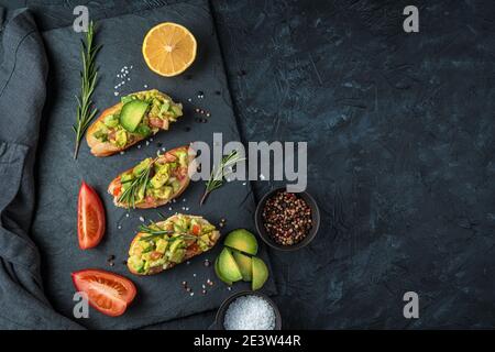 Eine kulinarische Kulisse mit Avocado-Sandwiches und frischem Gemüse auf einem schwarzen Betontisch. Stockfoto