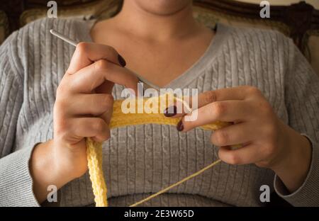 Die Frau strickt Wollkleidung. Stricknadeln. Nahaufnahme der Hände. Arbeiten Sie von zu Hause aus. Naturwolle. Stockfoto
