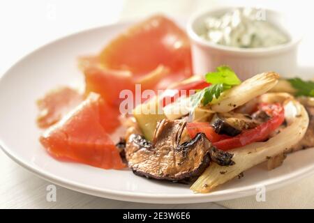 Mediterranes Ofengemüse wie Pilze, Fenchel und Paprika mit Petersilie garnieren, geräucherter Lachs und Dip auf einem weißen Teller, gesunde Low Carb Stockfoto