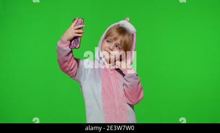 Kind Mädchen im Einhorn Pyjamas Kostüm mit Smartphone. Portrait von blonden Kind emotional macht Selfie auf Handy. Videoanruf, Blog, Spiele spielen, Handy ansehen. Mit lustigen Gesichtern Stockfoto