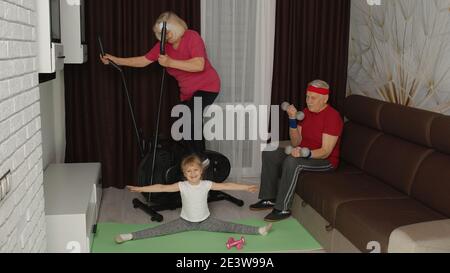 Ältere ältere ältere Paar Mann Frau mit Kind Mädchen mit orbitrek, dabei Gewichtheben Sport Hanteln und Stretching-Übungen Training zu Hause. Aktive alte Großeltern mit Enkelin beim Sport Stockfoto