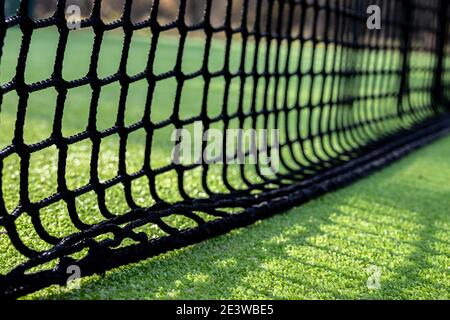 Selektiver Fokus eines schwarzen Netzes, um Paddel oder zu spielen Tennis auf grünem Kunstrasen Stockfoto