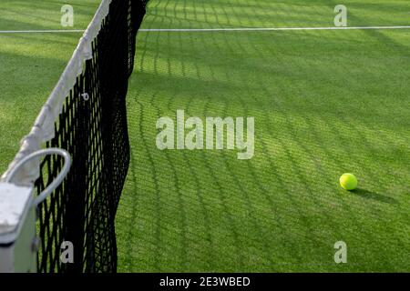 Selektiver Fokus eines schwarzen Netzes mit weißem Schutz Spielen Sie Paddel oder Tennis und einen Ball aus dem gleichen Spiel auf grünem Kunstrasen mit Kopierraum Stockfoto