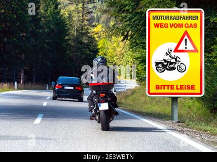 Fahrszene auf der Straße mit Motorradfahrer und Verkehrsschild 'Motorradfahrer weg vom Gas -Bitte leise-' (Motorradfahrer aus dem Gas - bitte ruhig) Stockfoto