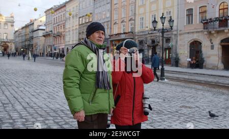 Ältere Rentner Paar Mann und Frau Touristen. Älterer Großvater fotografiert mit Großmutter auf Retro-Kamera. Familie genießen Urlaub Zeit zusammen in Winter verschneiten Stadt Lviv, Ukraine Stockfoto