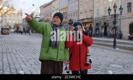 Stilvolle ältere ältere Paar Touristen Großmutter und Großvater reisen, fotografieren auf Retro-Kamera auf Winter City Straße. Schöne ältere Rentner Familienurlaub Weihnachtsferien Stockfoto
