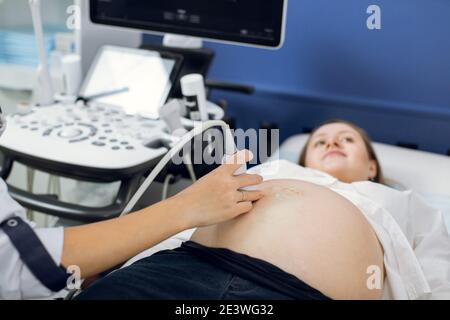 Schwangere Frau bekommen Ultraschall vom Arzt. Arzthand Durchführung Ultraschalluntersuchung des Bauches der jungen hübschen schwangeren Frau in modern Stockfoto