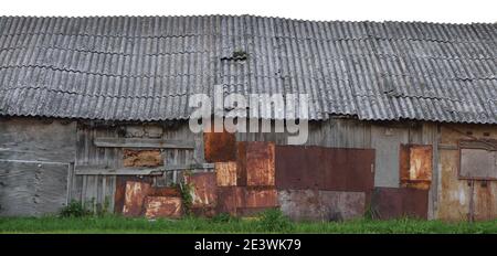 Alte verwitterte Holzhütte, grau überzogene Holz-Boarding-Hütte-Wand, geflickte Bretter, verrostete Metallplatten, rostige Farbstruktur, isoliertes Panorama Stockfoto