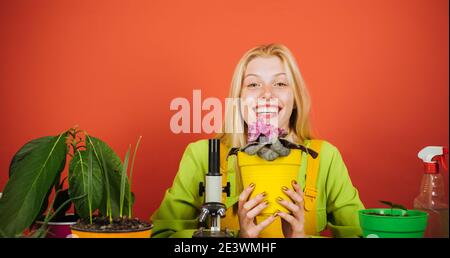 Happy Florist posiert mit Blume zur Kamera. Portrait der fröhlichen Dame im botanischen Garten. PIN up Mädchen mit blonden Haaren halten violett. Porträt von Smili Stockfoto