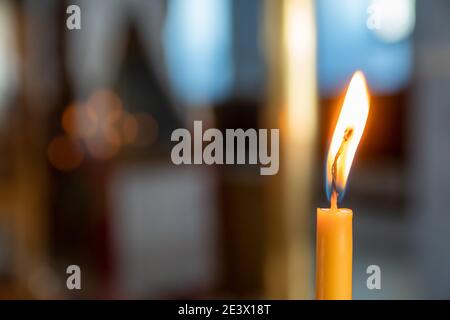 Festliches und religiöses Konzept: Nahaufnahme und Fokus auf eine einzelne gelbe Kerze mit heißer Flamme. Verschwommener Hintergrund Stockfoto