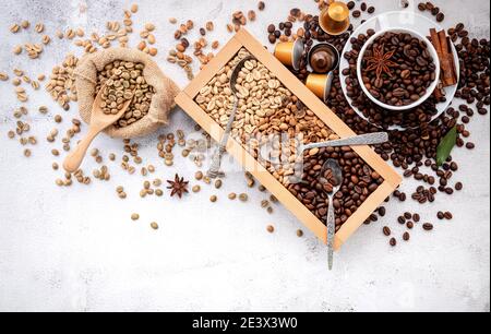 Grün und braun entkoffeiniert ungegeröstet und dunkel gerösteten Kaffeebohnen in Holzkiste mit Kugeln Setup auf weißem Beton Hintergrund. Stockfoto