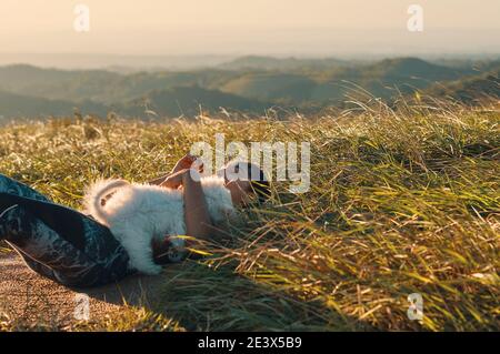 Eine Frau, die auf dem Gras liegt und ihren Welpen umarmt Hund nach dem Training Stockfoto
