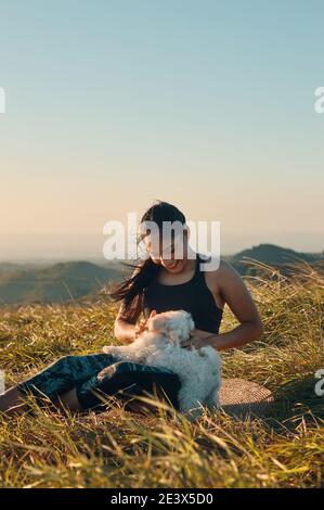 Eine glückliche junge Frau, die auf dem Gras sitzt und mit ihr spielt Ihr wunderschöner Welpenhund Stockfoto