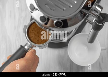 Der Prozess der Herstellung eines Espresso für eine Kaffeepause. Draufsicht auf eine Hand, die einen Portafilter einer Kaffeemaschine mit gemahlenem Kaffee hält. Stockfoto