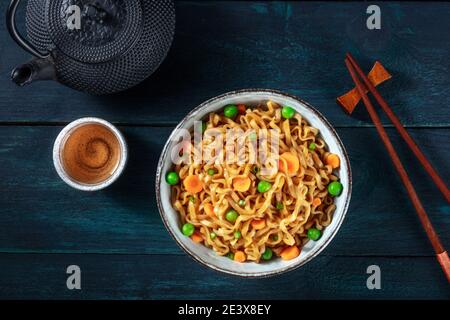 Nudeln mit Gemüse und Tee, oben flach lag auf einem dunkelblauen Holzhintergrund erschossen Stockfoto