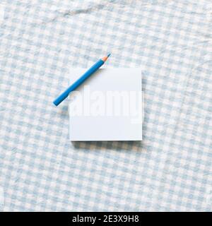 Blaues Notizblock mit Farbstift auf blauem Karomuster Stoff Hintergrund. Draufsicht, Kopierraum Stockfoto
