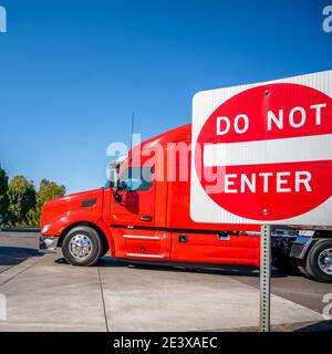 Leuchtend rote Industrie leistungsstarke große Rig Motorhaube semi-Truck mit Hochkabine für Langstreckentransport mit Sattelaufliegern An der Stadtstraße mit Stockfoto