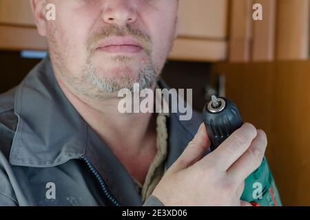 Montage und Reparatur von Möbeln. Ein Mann in grauer und roter Spezialkleidung für die Arbeit mit einem Schraubendreher in den Händen. Nahaufnahme, selektiver Fokus. Stockfoto