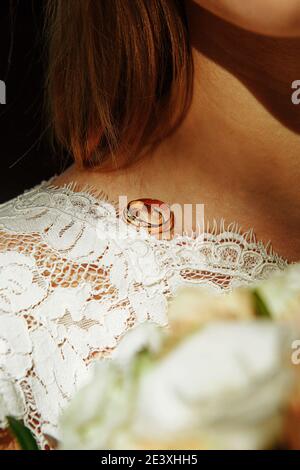 Ein Paar Eheringe der Braut und des Bräutigams auf der Schulter der zukünftigen Frau in einem weißen Kleid. Hochzeitszubehör, Zeremonie, Schmuck, Bridal bou Stockfoto