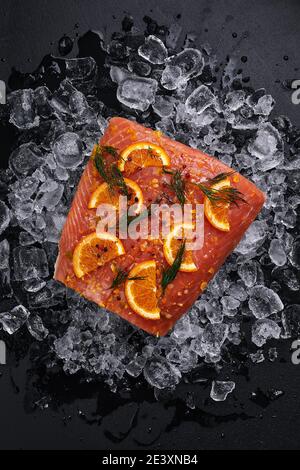 Rohes Lachsfilet mit Orangenscheiben auf Eisstücken Auf schwarzem Hintergrund Stockfoto