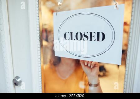 Nahaufnahme einer Geschäftsbesitzerin, die ein nahes Schild an der Tür ihres Ladens aufgehängt hat. Weibliche Besitzerin, die ein geschlossenes Schild an die Eingangstür ihres Bekleidungsladens legte. Stockfoto