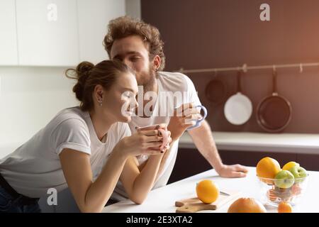 Morgenkaffee und sanfte Küssen Fütterung einander Spaß in der modernen Küche und lächeln beim Kochen zu Hause. Hübsches Mädchen füttert oder stillt sie Stockfoto