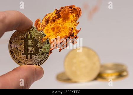 bitcoin zwischen zwei Fingern mit heißem Feuer auf dem gehalten Münze mit anderen Münzen im Hintergrund Stockfoto