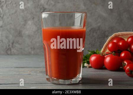 Hohes Glas Tomatensaft mit reifen Tomaten auf einem grauen Holztisch, ein klassischer Tomatensaft in einer einfachen Szene Stockfoto