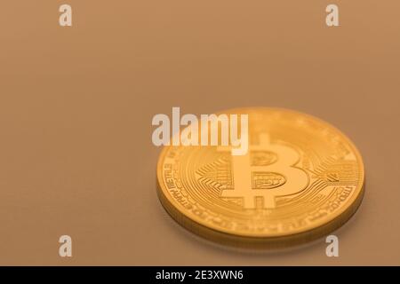 Eine einzelne goldene Bitcoin, die auf einem orangefarbenen weichen Hintergrund liegt Stockfoto