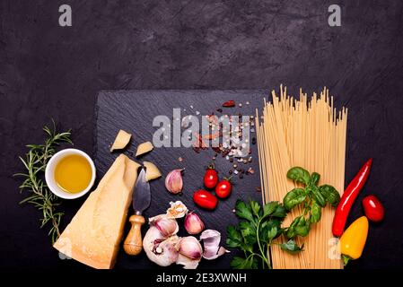 Italienische Küche: Auf einem Schieferstein, rohe Spaghetti, gereiften Grana Padano Käse, Knoblauch, Öl und zahlreiche Zutaten mit aromatischen Kräutern. Blick von oben Stockfoto