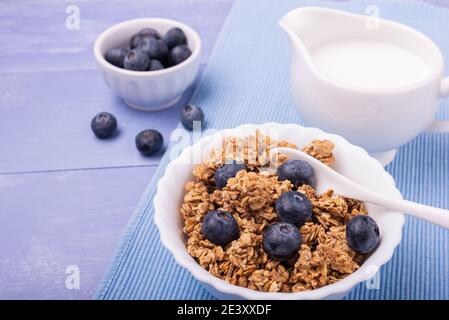 Auf dem Lavendelblauen Tisch, gesundes Frühstück mit knusprigen Vollkornmüsli aus Gerste und Hafer, Heidelbeeren und frischer Milch. Stockfoto