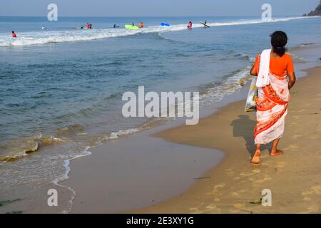 Kulturelle Gegenüberstellung, Surfers, Indian Lady in Sari Spaziergang am Varkala Beach, Varkala, Kerala, Indien Stockfoto