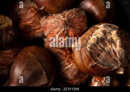 Haufen gerösteter Edelkastanien auf dunklem Hintergrund. Geschälte Kastanien und Nußschale. Draufsicht, Vollformat-Makroaufnahme. Dunkel und launisch. Stockfoto