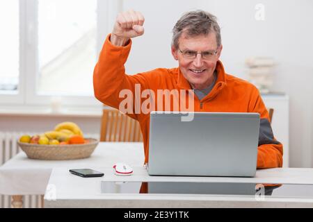 Glücklicher reifer Mann, der von zu Hause aus mit einem Laptop arbeitet Stockfoto