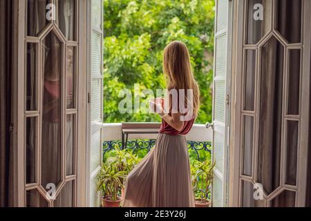 Eine rothaarige Frau steht auf einem Balkon im traditionellen Stil und genießt ihren Morgenkaffee. Eine Frau in einem Hotel in Europa oder Asien als Tourismus erholt sich von einem Stockfoto